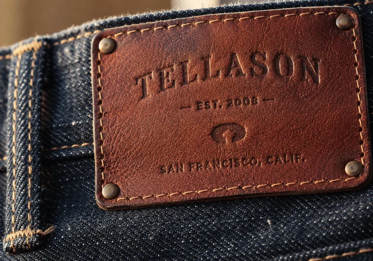 Debossed leather patch with sew-on stitching and rivets on denim jeans
